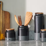The Cole & Mason Linton Ceramic Utensil Pot holds cooking tools on a marble countertop beside a wooden cutting board, set against a light-colored wall.