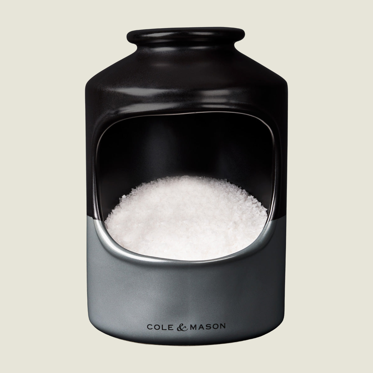 A ceramic salt cellar with a wide opening, filled with coarse sea salt. The container is black and gray with Cole & Mason printed on the front.