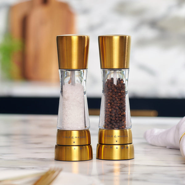 Modern Cole & Mason gold stainless steel and acrylic  salt and pepper grinders with adjustable grind settings on a kitchen counter