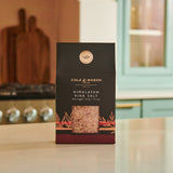 A Cole & Mason Pink Himalayan Salt Box sits on a kitchen counter, ideal for refilling your salt mills—a gourmet cooking essential, with a stove and pastel blue cabinets softly blurred in the background.