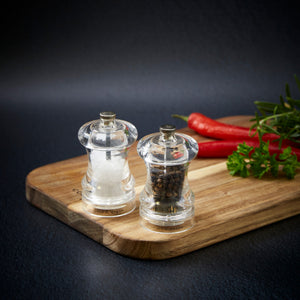 #85mm#pepper
Two Cole & Mason Acrylic Capstan Salt & Pepper Mills with a clear design rest on a wooden board, surrounded by red chili peppers, parsley, and rosemary against a dark background.