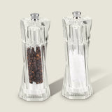 The Cole & Mason Aldeburgh Salt & Pepper Mill Set features two clear acrylic mills with adjustable grinding, filled with black peppercorns and coarse sea salt, standing side by side on a light background.