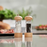 The Cole & Mason Basics Wood Salt & Pepper Mill Set features two clear grinders with durable wood tops and bases, filled with coarse salt and whole peppercorns, plus adjustable grind settings for personalized seasoning.