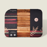 The rectangular Berden Acacia Carving Board by Cole & Mason comes partially wrapped in stylish packaging with black, red, and beige foliage patterns—an elegant addition to your kitchen.