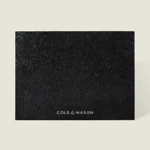 The Cole & Mason Black Granite Surface Protector features a square, textured black granite design with the brand name printed in white—an elegant and heat-resistant addition to your kitchen décor.