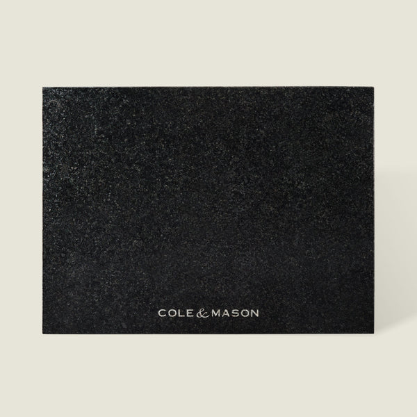 The Cole & Mason Black Granite Surface Protector features a square, textured black granite design with the brand name printed in white—an elegant and heat-resistant addition to your kitchen décor.