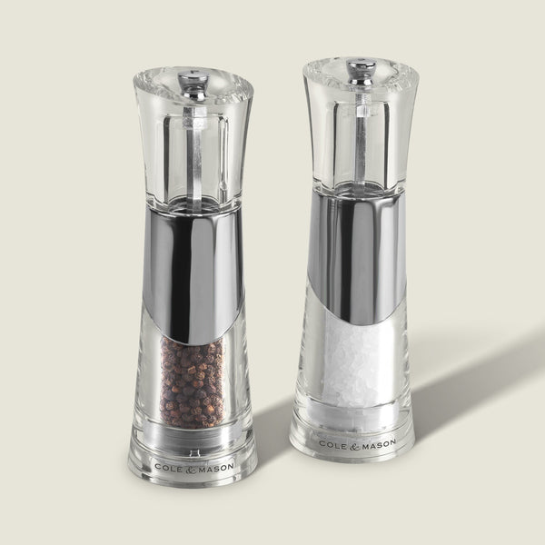 The Cole & Mason Bobbi Salt & Pepper Mill Set features two clear, modern mills with silver accents, adjustable grinders, and durable mechanisms. Each is prefilled with black peppercorns or coarse sea salt and labeled Cole & Mason at the base.