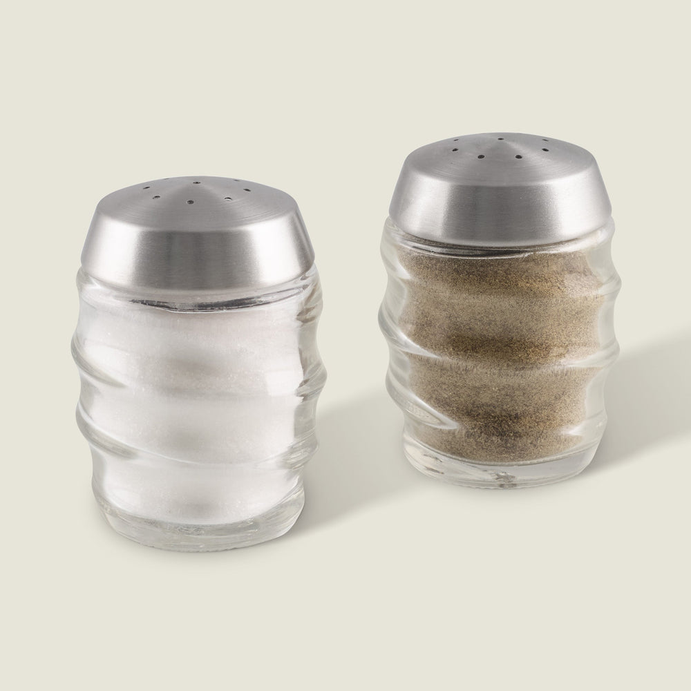 The Cole & Mason Bray Glass Shakers Set features two clear glass shakers with stainless steel tops and a wavy design—one for salt, one for pepper—placed side by side, ideal for any kitchen décor.