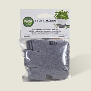 A set of gray, cross-shaped absorbent pads from Cole & Mason UK for the Burwell Self Watering Potted Herb Keeper Small and Tealby Herb Keeper, visible in clear packaging with branded labels and herb illustrations.