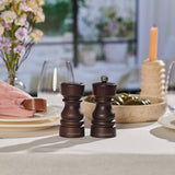 A set dining table with a pink napkin, stacked plates, Cole & Mason London Chocolate Wood Salt Shaker & Pepper Mill Set featuring grind select technology, glassware, a beige candle, and a floral centerpiece on a cream tablecloth.
