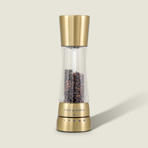 The Cole & Mason Derwent Gold Salt & Pepper Mill features gold-tone stainless steel, advanced grinding technology, and is filled with black peppercorns, all set against a plain, light background.