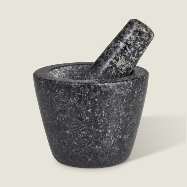 The Cole & Mason Dorchester Granite Pestle & Mortar, in dark gray with speckled detail, sits on a light background. The pestle rests inside the bowl, angled right—ideal for grinding herbs or making fresh spice blends.