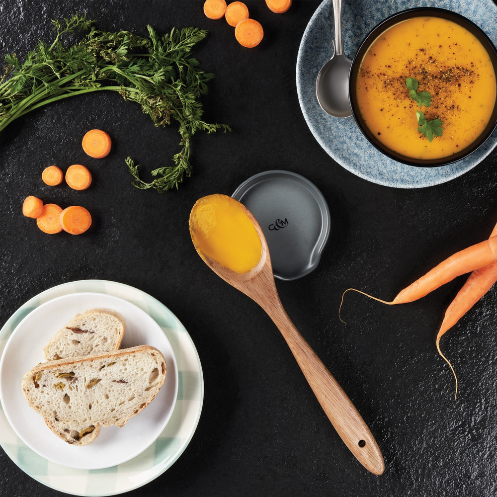 The Cole & Mason Duxford Ceramic Spoon Rest is a black, round ceramic piece with a raised edge and front cutout—perfect for kitchen decor and shown against a light cream background.