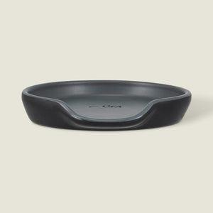 The Cole & Mason Duxford Ceramic Spoon Rest is a black, round ceramic piece with a raised edge and front cutout—perfect for kitchen decor and shown against a light cream background.