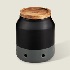 The Cole & Mason Elmdon Ceramic Garlic Keeper, in black and gray with a wooden lid and round ventilation holes, offers stylish garlic storage and appears against a light background.
