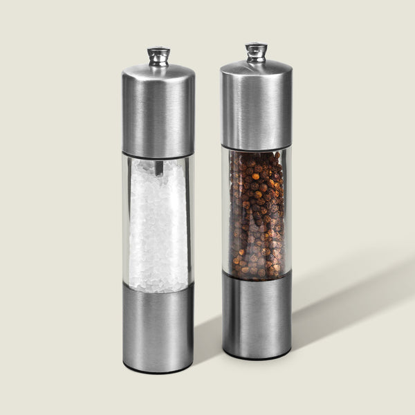 The Cole & Mason Everyday Stainless Steel Salt & Pepper Mill Set features an ergonomic design and adjustable coarseness; both mills stand upright on a light background, one containing coarse salt, the other whole black peppercorns.