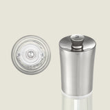 An upright Cole & Mason Everyday Style Salt & Pepper Mill Set salt grinder with a transparent base and adjustable settings stands in a kitchen. Beside it, the ceramic grinding mechanism is shown from above on a light background.