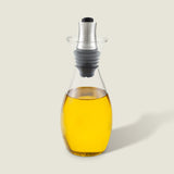 The Cole & Mason Haverhill Oil & Vinegar Pourer, filled with golden yellow oil, has a silver and black precision pour spout for drip-free use and is displayed against a light gray background.