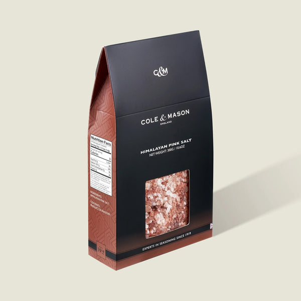The Cole & Mason Pink Himalayan Salt Box features a clear window showing vibrant salt crystals. Its brown and black box with white text is ideal for refilling salt mills and provides nutritional info on the side.