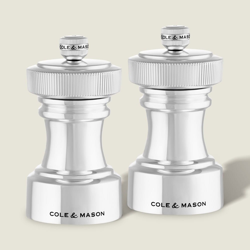 The Cole & Mason Hoxton Silver Plated Salt & Pepper Mill Set stands side by side on a light background, showcasing a sleek, modern design with ribbed tops and compact bases—ideal for elegant dining.