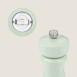 A pastel green Kenton Sage Salt & Pepper Mill by Cole & Mason is shown, highlighting its ceramic mechanism and branded design. The top features a silver, interchangeable knob marked with a P.