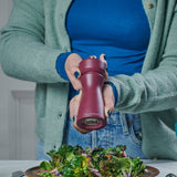 A person in a green cardigan and blue shirt uses the Cole & Mason Kenton Salt & Pepper Mill in Sichuan Pepper to season a bowl of salad greens.