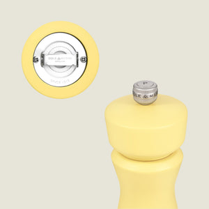 A close-up of the Cole & Mason Kenton Salt & Pepper Mill in Turmeric Yellow features a silver P knob and an inset highlighting its durable ceramic grinder marked with the brand name.