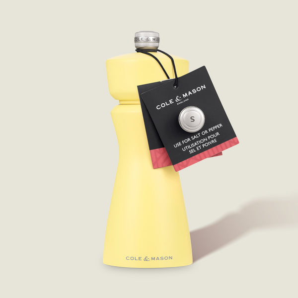 The Cole & Mason Kenton Salt & Pepper Mill in Turmeric Yellow features a silver top, ceramic mechanism, and black tag indicating its suitable for salt and pepper. Stands upright on a light background.