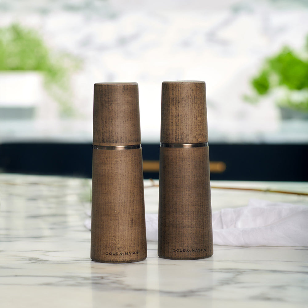 Two Marlow Grey Beech Salt & Pepper Mills by Cole & Mason UK, featuring a smooth tapered shape and wood grain, stand upright on a light background with an adjustable grinding mechanism for custom seasoning.