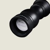 Close-up of a black Cole & Mason Southwold Capstan Salt & Pepper Mill on its side, showing the white ceramic grinder. Features durable build and adjustable grind, set against a smooth, light beige background.