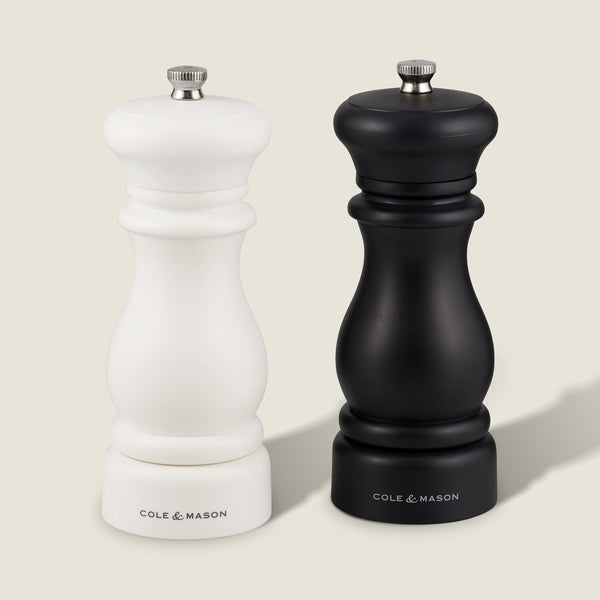 A white and black Cole & Mason Southwold Capstan Salt & Pepper Mill set, featuring a classic hourglass shape and sturdy build, are displayed side by side on a light background.