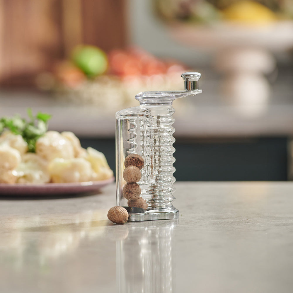 The Cole & Mason Wallis Professional Nutmeg Grinder is a clear glass grinder with an ergonomic design, stainless steel blade, metal crank handle, vertical spiral mechanism, and side storage for whole nutmeg.