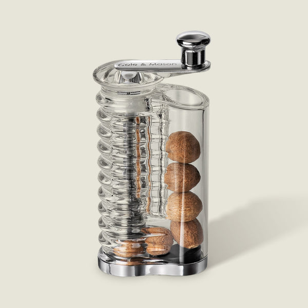 The Cole & Mason Wallis Professional Nutmeg Grinder is a clear glass grinder with an ergonomic design, stainless steel blade, metal crank handle, vertical spiral mechanism, and side storage for whole nutmeg.